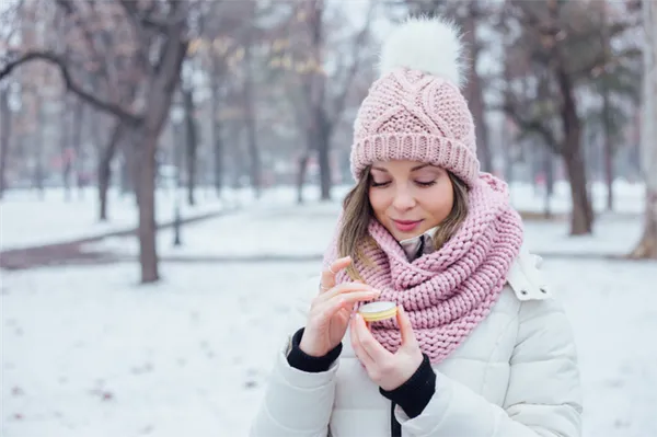 Девушка в зимнем парке наносит кокосовое масло на кожу губ.